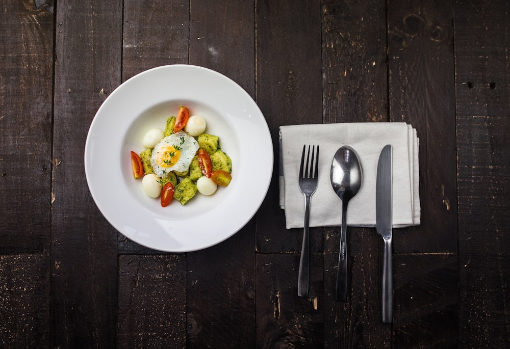 sunny side up egg, boiled quail eggs, sliced red tomatoes, and sliced green bell pepper inside round white ceramic plate in a fine dining set