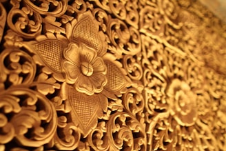 Ornate wooden carving featuring intricate floral and geometric patterns, with a prominent flower motif at the center. The craftsmanship showcases detailed vines and leaves, meticulously chiseled to create a rich tapestry of natural elements.