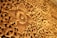 Ornate wooden carving featuring intricate floral and geometric patterns, with a prominent flower motif at the center. The craftsmanship showcases detailed vines and leaves, meticulously chiseled to create a rich tapestry of natural elements.