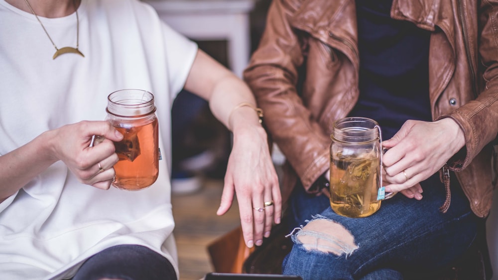 two person sitting while holding clear glass mason mugs