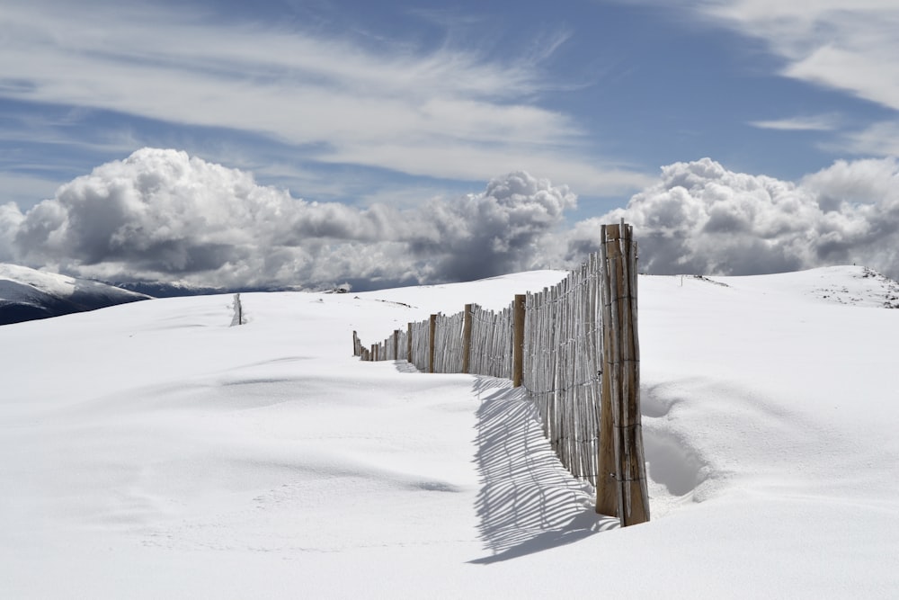 recinzione di legno marrone sul campo di neve sotto nuvole grigie