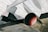 The image depicts a close-up view of a jet aircraft's engine and exhaust area. The aircraft is metallic and appears to be housed in a large hangar or museum with a grid-like ceiling structure. Part of an insignia or logo is visible on the aircraft's body.