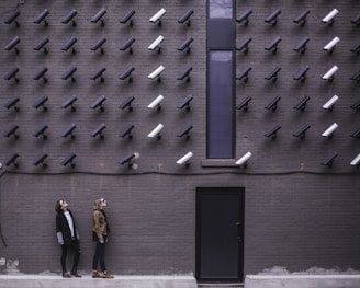 two women facing security camera above mounted on structure