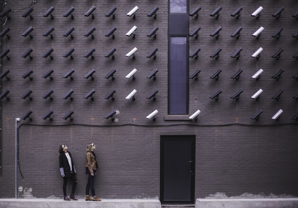 two women facing security camera above mounted on structure