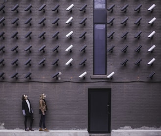 two women facing security camera above mounted on structure