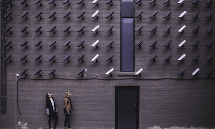 two women facing security camera above mounted on structure