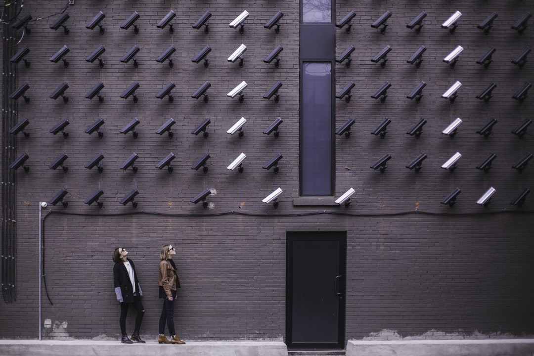 two women facing security camera above mounted on structure, Women look at security cameras