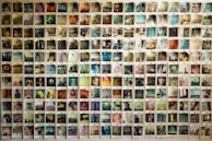 A large collection of Polaroid photos are displayed on a wall, each capturing different scenes and subjects such as landscapes, portraits, and abstract images. The photos are arranged systematically in a grid format, creating a visually engaging collage with various colors and themes.
