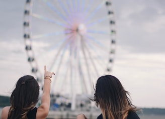 two women sitting on bench pointing white and blue Ferris wheel