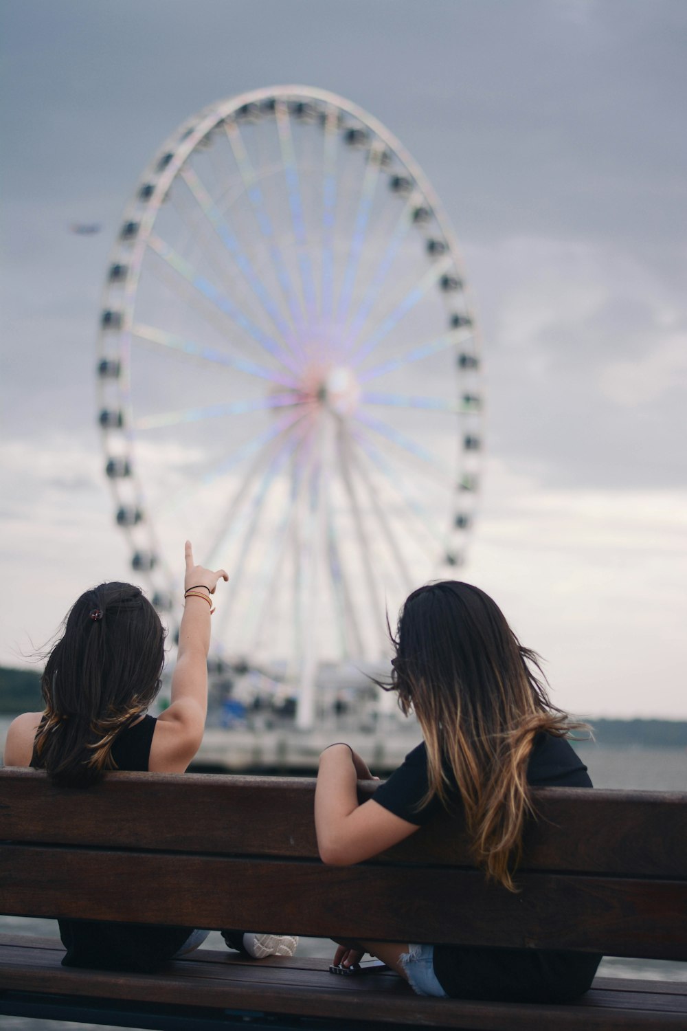 zwei Frauen sitzen auf einer Bank und zeigen auf ein weiß-blaues Riesenrad