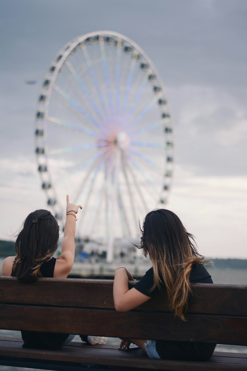 two women sitting on bench pointing white and blue Ferris wheel