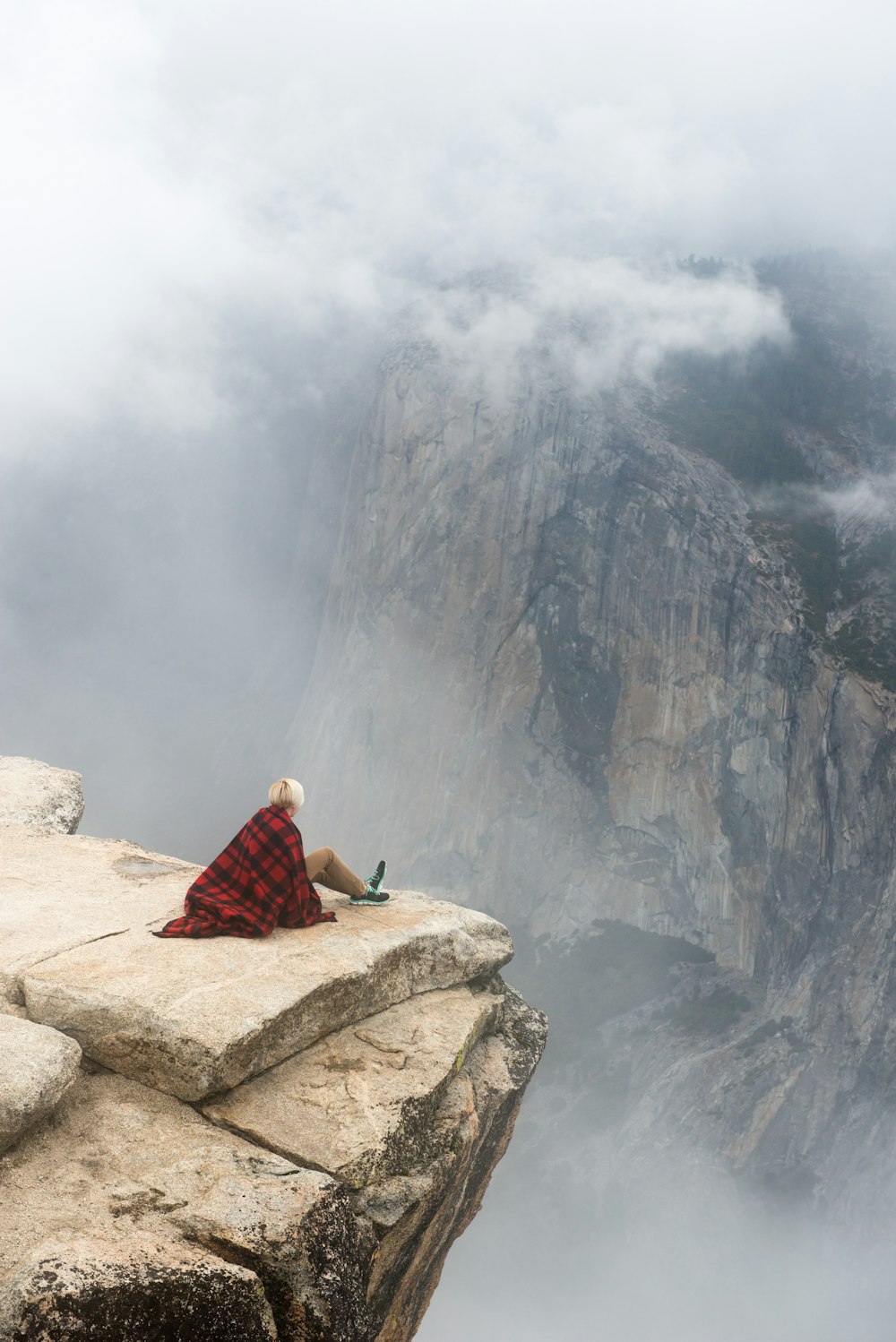 Hiker sits on the rocky ledge of a high mountain in Yosemite National Park