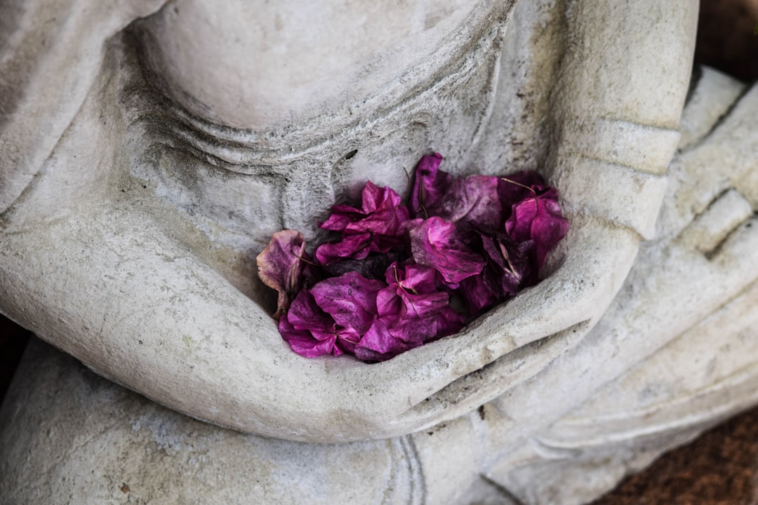 A bunch of purple flowers in the hands of a statue of a person sitting cross-legged