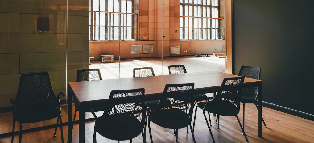 A sleek conference room with a polished wooden table and leather chairs, sunlight streaming through large windows.