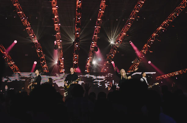 The band performing live on stage with colorful lights and an enthusiastic crowd.