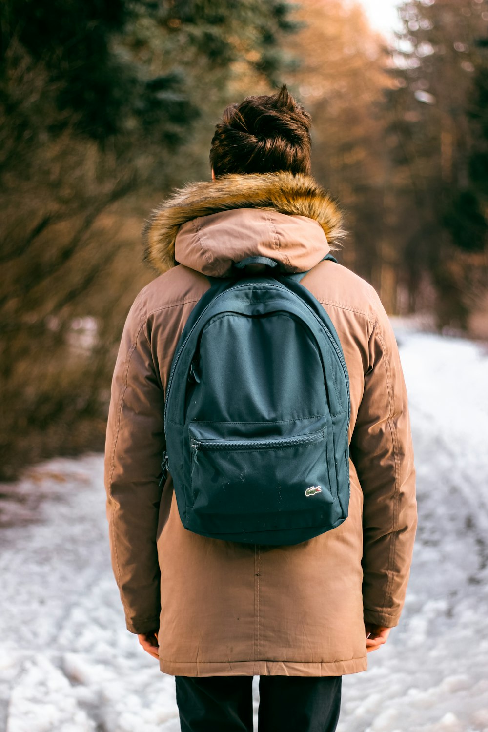 Rückenfoto einer Frau, die einen braunen Parka-Kapuzenpullover und einen grünen Rucksack auf Schnee trägt