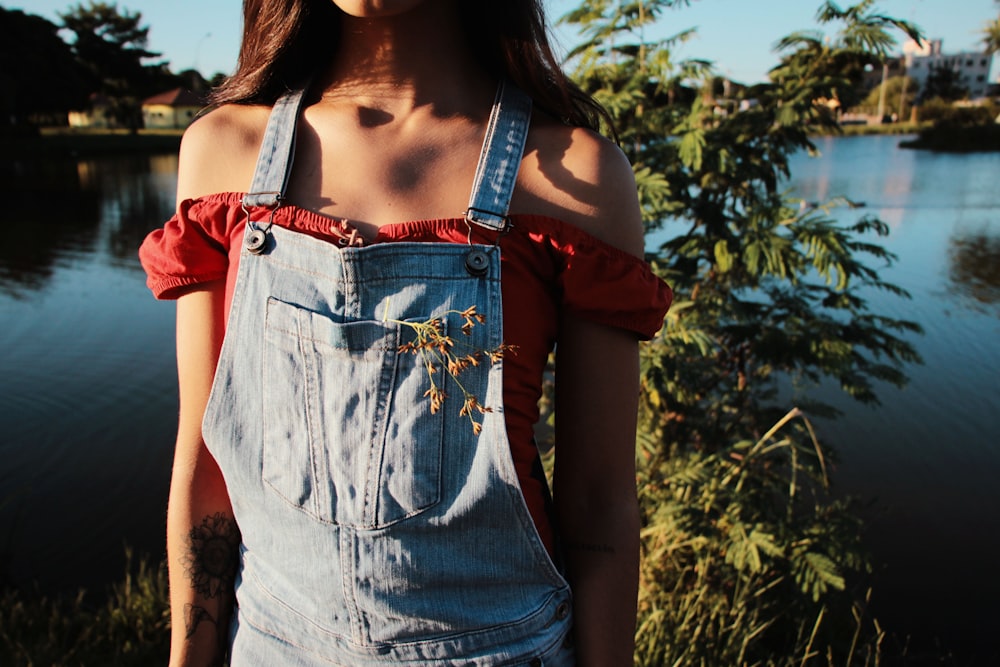 a woman wearing a denim overalls standing next to a lake