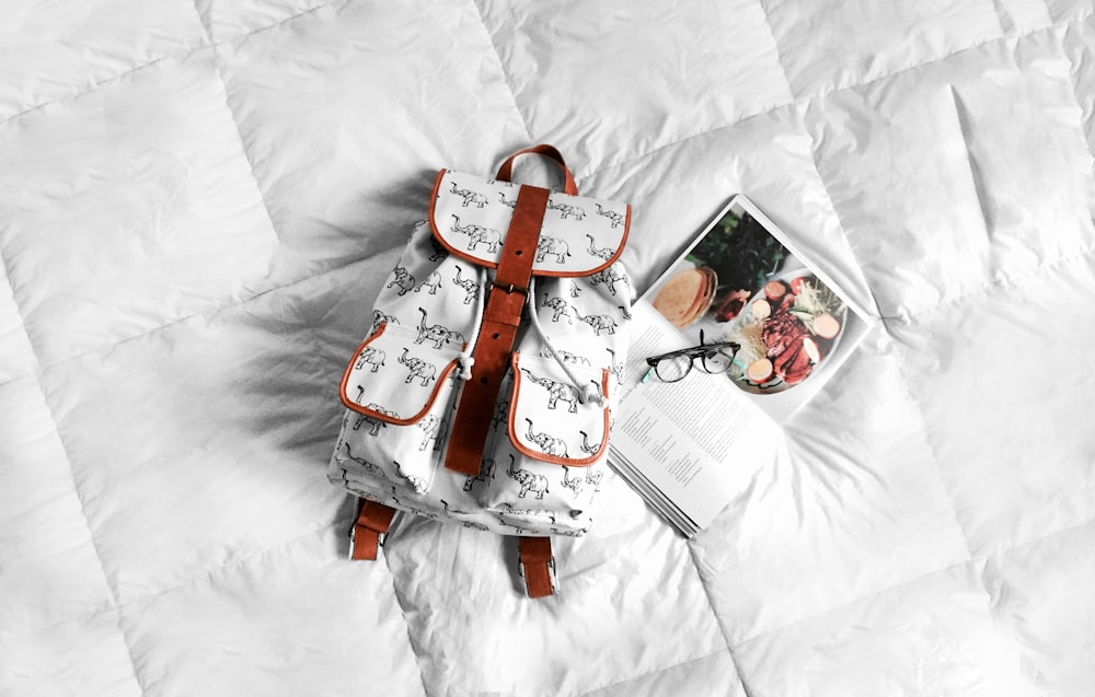 ベッドの上の白と茶色の革のバッグ