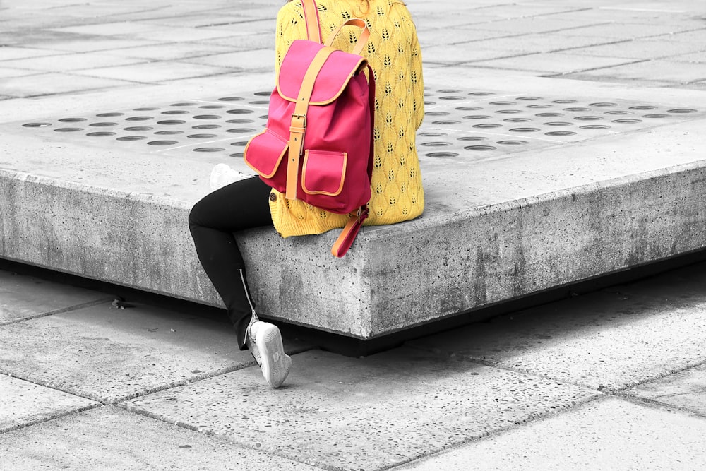 woman carrying pink backpack sitting on the edge concrete bracket