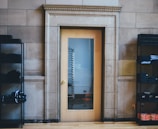 A wooden door with a glass panel in a stone wall, flanked by black metal shelving units holding neatly folded clothes. The door reflects a metal rack through the glass.