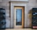 A wooden door with a glass panel in a stone wall, flanked by black metal shelving units holding neatly folded clothes. The door reflects a metal rack through the glass.