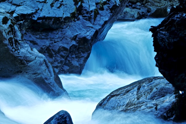 Icy glacial water cascading over smooth rocks with electric blue hues.