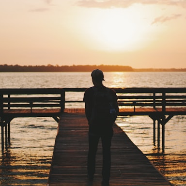 silhouette of man walking on dock during golden hour