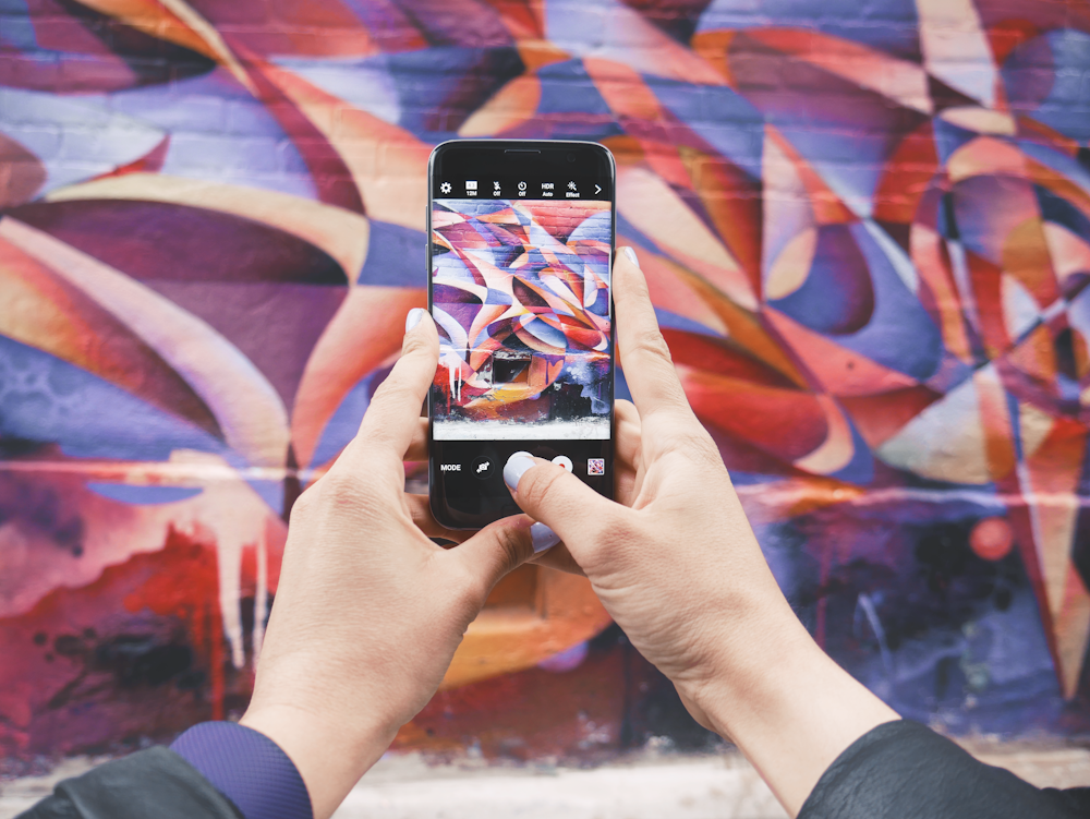 Androidスマートフォンを持ち、昼間、抽象的な壁の写真を撮る人