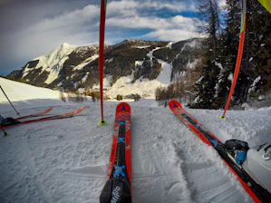 Close-up of ski equipment resting on fresh snow with mountain peaks blurred in the background.