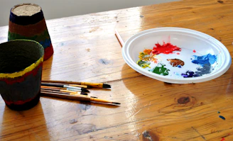 An array of colorful glazes drying on a wooden workshop table with brushes.