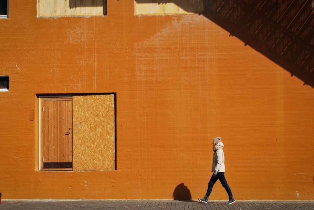 man walking beside orange building at daytime