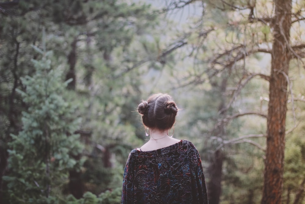 woman standing facing green forest