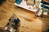 A retail clothing store with a wooden floor. A display table shows neatly folded clothes and decorative items, while a mannequin is dressed in patterned clothing. A circular clothing rack holds various-colored garments on hangers.