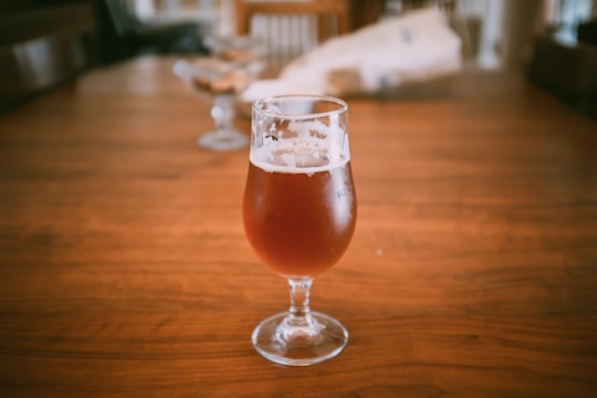 Close-up of a frosty glass of amber IPA beer with citrus peel garnish on a wooden table.