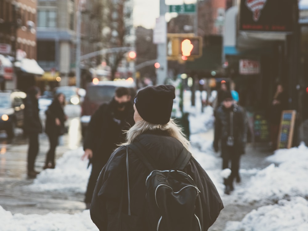 woman carrying backpack standing beside snow on street at daytime