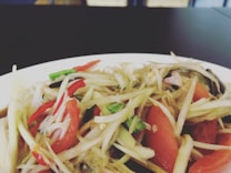 A close-up of a plate filled with a vibrant salad featuring thinly sliced green papaya, red and green chili peppers, tomatoes, and other vegetables. The ingredients are fresh and finely chopped, creating a colorful and appetizing dish.