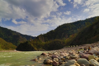 A serene river flowing through Kyrgyzstan mountains with a group practicing yoga on the riverbank.