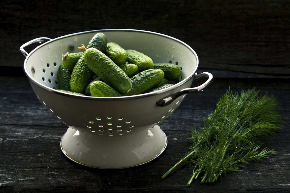 Pickle ingredients including dill garlic and salt laid out in a bowl and strainer
