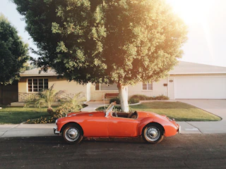 A shiny red sedan parked in front of a cozy suburban house on a sunny day.