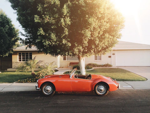 A shiny red sedan parked in front of a cozy suburban house on a sunny day.