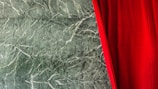 A luxurious deep red velvet curtain partially covers a background of textured green marble. The marble features intricate white veining, adding a sophisticated touch to the scene.