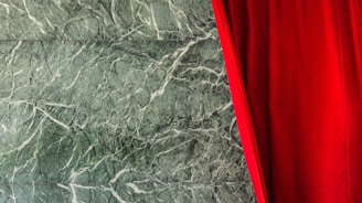 A luxurious deep red velvet curtain partially covers a background of textured green marble. The marble features intricate white veining, adding a sophisticated touch to the scene.