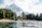 A serene alpine scene featuring a snow-capped mountain in the background, lush evergreen trees, and a tranquil lake in the foreground. A cozy wooden cabin is nestled among the trees, providing a picturesque and peaceful retreat setting.