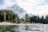 A serene alpine scene featuring a snow-capped mountain in the background, lush evergreen trees, and a tranquil lake in the foreground. A cozy wooden cabin is nestled among the trees, providing a picturesque and peaceful retreat setting.
