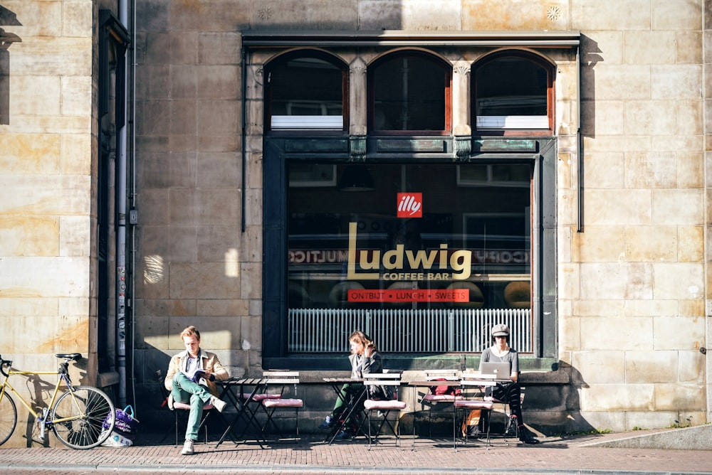 tres personas sentadas en una silla al aire libre frente a la cafetería Ludwig