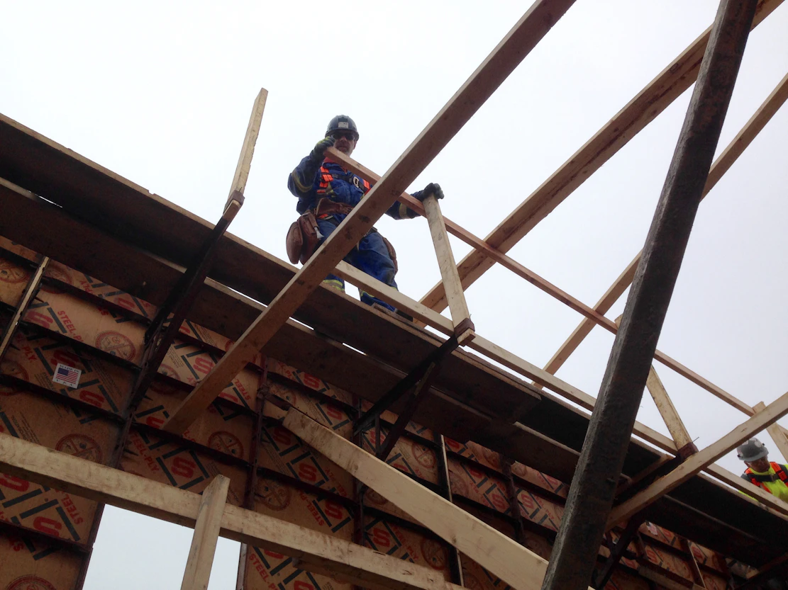 A safety trainer assisting a worker with a harness on a construction site.