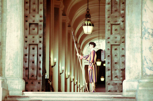 A security guard in deep crimson uniform attentively monitoring a modern office lobby.