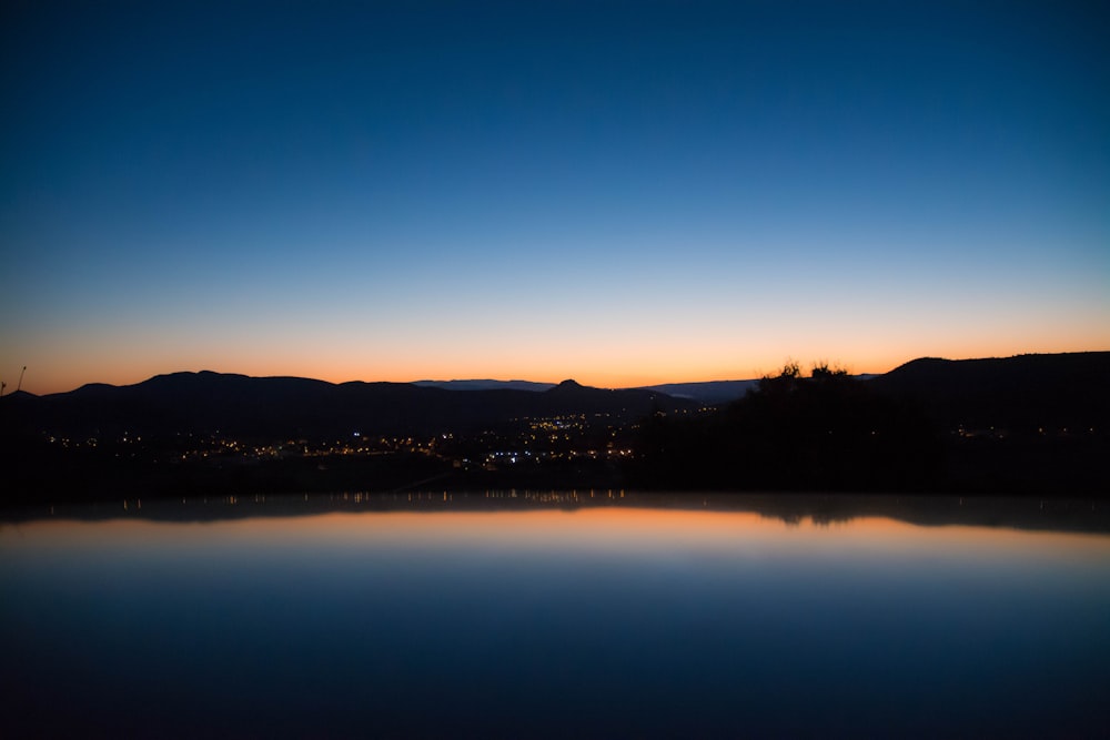 calm lake waters reflecting city and trees and clear sky