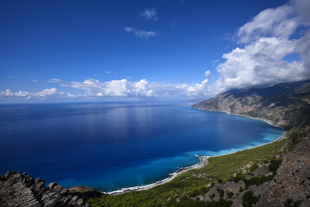 blue ocean water beside mountain under blue and white cloudy sky