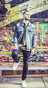 Model wearing a premium blue bomber jacket with black details, standing against a graffiti wall.